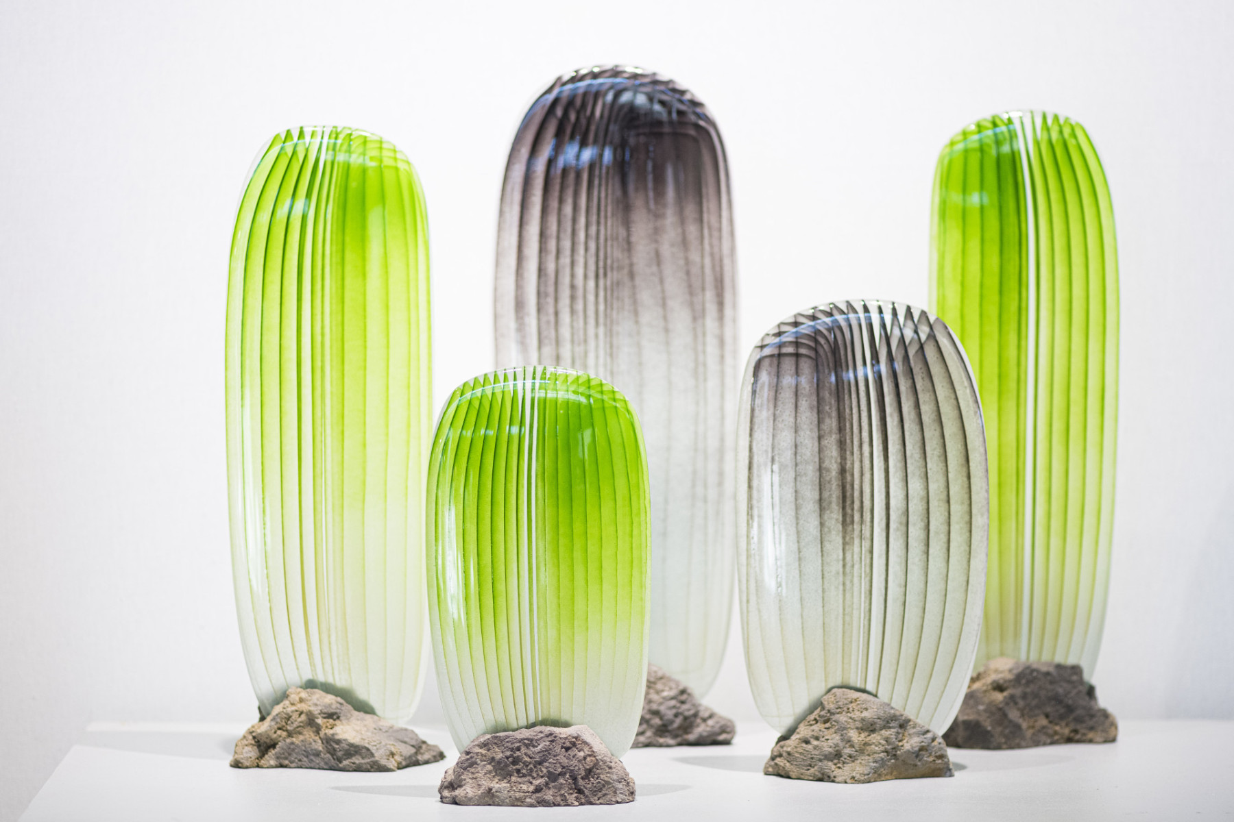 Sculptures de verre réalisées en dégradé de couleurs vertes serti sur une roche volcanique, à l'aspect brut et rugueux de Jonathan Ausseresse, présentées sur le salon Maison & Objet en 2022.